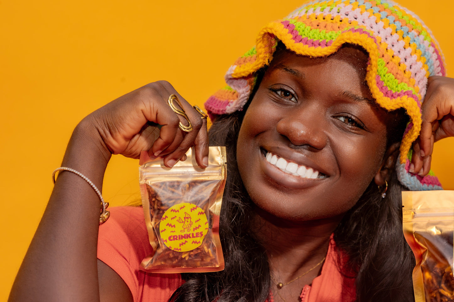 Woman holding bags of Crinkles plantain chips against a yellow background