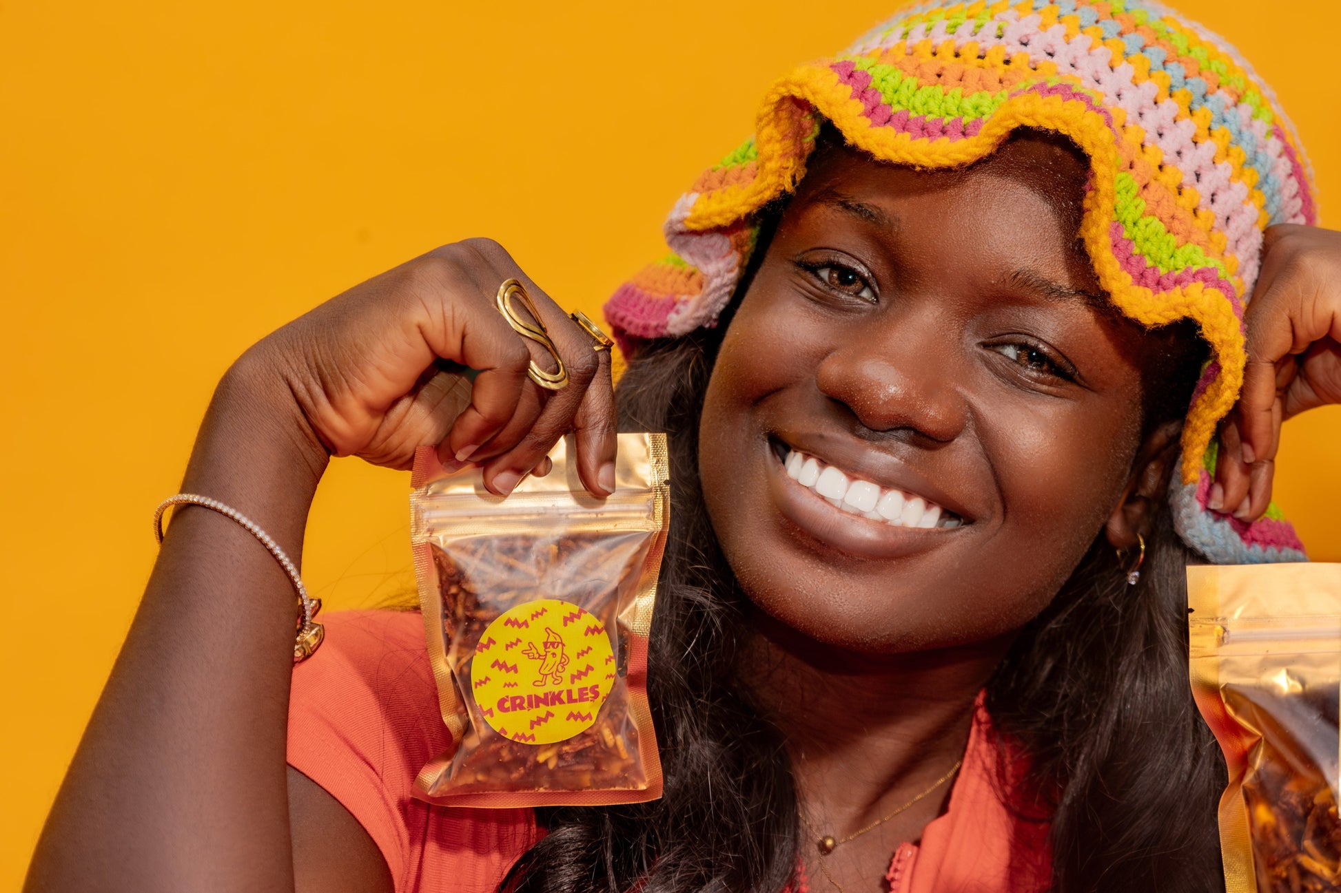 Woman holding bags of Crinkles plantain chips against a yellow background